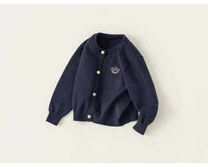 Détail du cardigan bleu marine avec boutons dorés et écusson brodé sur une maille de qualité