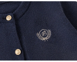 Détail macro du cardigan en maille bleu marine avec boutons dorés et blason brodé