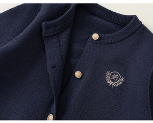 Détail d'un cardigan en maille bleu marine avec broderie de laurier et boutons dorés