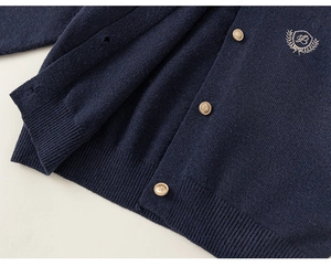 Détail du cardigan en maille bleu marine avec boutons dorés et blason brodé chic