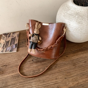 Bruine vintage emmertas met goudkleurige hardware en konijnenhanger op houten tafel