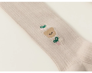 Detail of ribbed knit leggings featuring a cute brown bear embroidery and floral accents