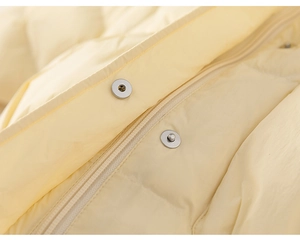 Detailed macro view of yellow down jacket showing metal snaps and windproof zipper closure