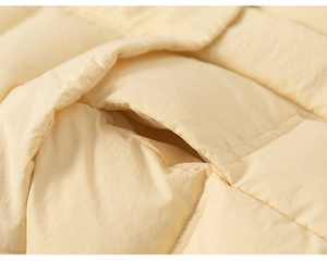 Detail of a yellow quilted down coat showing hand pocket stitching and windproof fabric