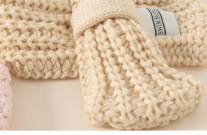 Dettaglio della trama della sciarpa in maglia beige con etichetta tessuta