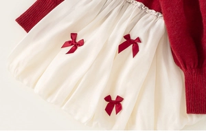 Detail eines roten Strickkleides mit weißem Satinfaltenrock und roten Seifenschleifen