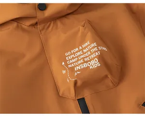 Detail of brown kids windbreaker featuring utility pocket with outdoor hiking typography