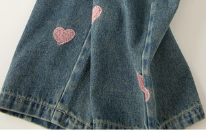 Detail shot of blue denim fabric with fine pink heart embroidery and neat stitching