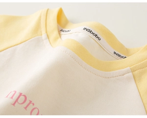 Detail eines Baby-T-Shirts mit Rundhalsausschnitt in Creme und Gelb mit Strickstruktur