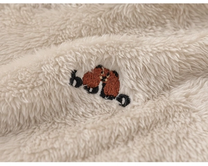 Close-up of soft cream fleece fabric with a cute brown bear embroidery detail