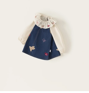 Détail du col à volants et broderie d'ours sur chemise crème avec robe en jean
