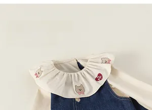 Détail du col à volants avec broderie ours et nœuds sur la robe en denim bleu
