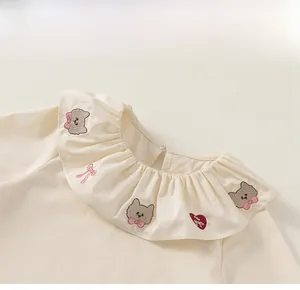 Détail d'un chemisier beige en coton pour filles avec col poupée et broderie chat