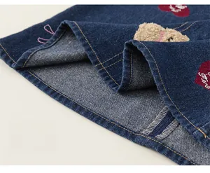 Détail de l'ourlet en denim avec écussons brodés de cœur et d'ours et surpiqûres orange
