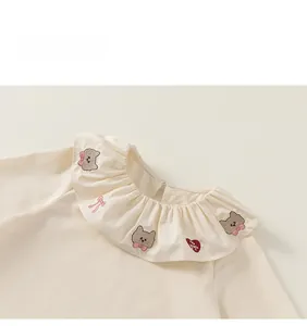 Détail du col Claudine avec broderie d'ours et de cœurs sur tissu en coton beige doux