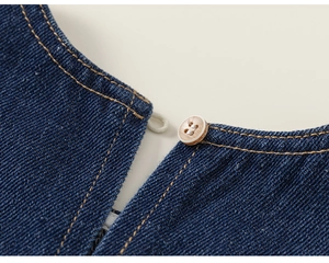Détail d'une robe en jean bleu foncé avec bouton en bois, boucle blanche et coutures jaunes