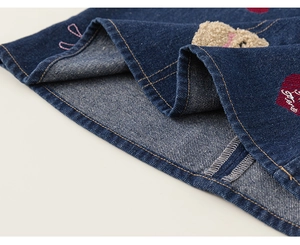 Détail de robe en jean avec écusson d'ours, nœud rose et broderie de cœur rouge