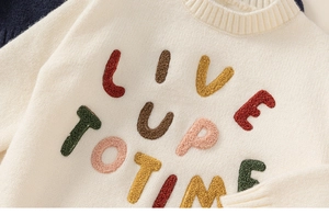 Close-up of white knit sweater featuring colorful chenille embroidery and ribbed neckline