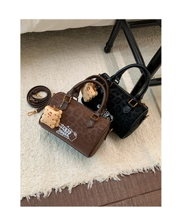 Detail view of coffee and black Boston bags with leopard texture and plush charms