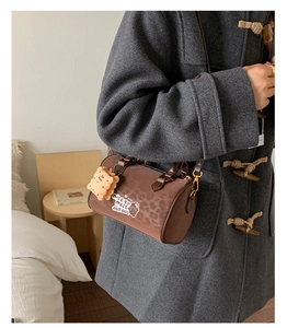 Detail of a brown leopard print cylinder bag with a plush bear charm and gold hardware