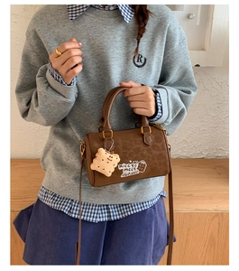 Close-up of brown leopard print Boston bag with plush biscuit charm and golden hardware