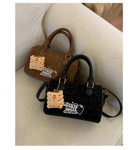 Close-up of leopard print suede Boston bag with cookie charm and logo detail on a sofa