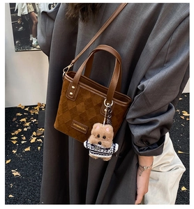 Close-up of brown suede bucket bag with woven texture, leather strap and teddy bear charm