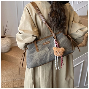 Detail van grijze denim schoudertas met lederen afwerking en bruine pluche beer hanger