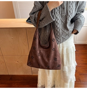 Detail of dark brown suede tote bag with laser-cut floral patterns and leather strap