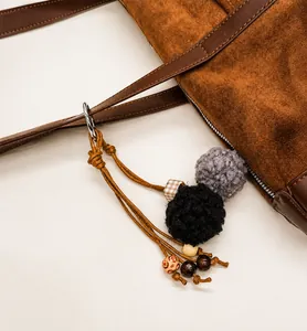Detail of grey and black plush pompoms with checkered beads on brown suede bag