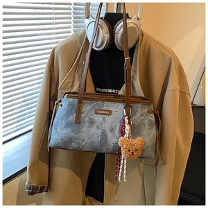 Detail van blauwe denim tas met bruine lederen handgrepen en schattige berenhanger
