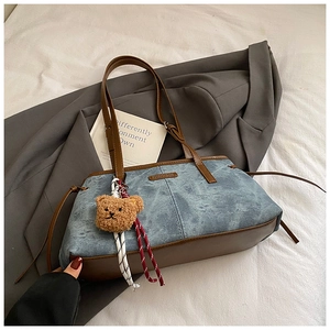 Detail van blauwe denim draagtas met bruine lederen basis en schattige teddybeerhanger