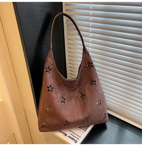 Detail view of brown suede tote bag with laser-cut floral patterns on a windowsill