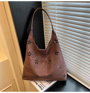 Detailed macro view of laser-cut floral patterns on brown suede hobo tote bag