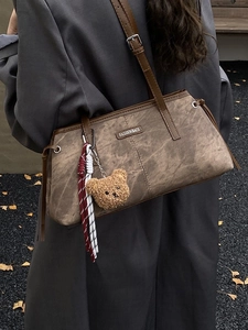 Vintage bruine matte leren schoudertas met berenhanger gedragen door een model