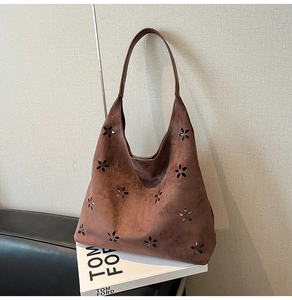 Detail of laser-cut floral pattern on brown suede tote bag with leather shoulder strap