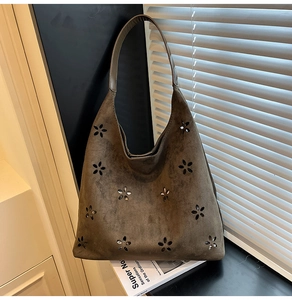 Close-up of brown suede hobo bag with laser-cut floral patterns on a magazine