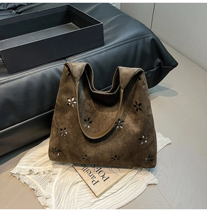 Detail of laser-cut flower patterns on dark brown suede tote with gold metal handles