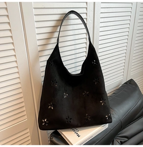 Detail of black suede tote bag with laser-cut floral patterns and metallic accents