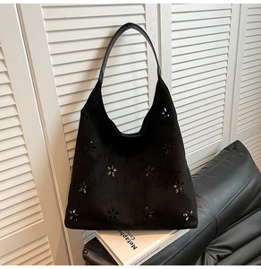 Detail view of black faux suede tote bag featuring hollow floral patterns and silver studs