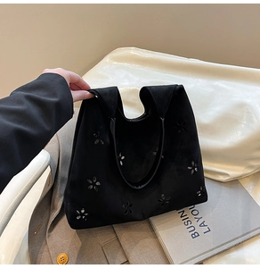 Detail view of black faux suede tote bag with laser-cut floral patterns on a desk