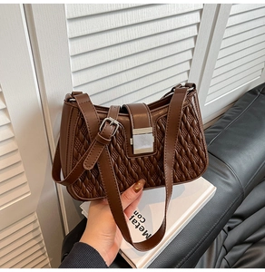 Detail of deep brown quilted leather texture and square metal clasp on a stylish handbag