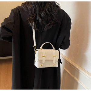 Detail van een witte glanzende crossbodytas met gouden gesp op een zwarte jas