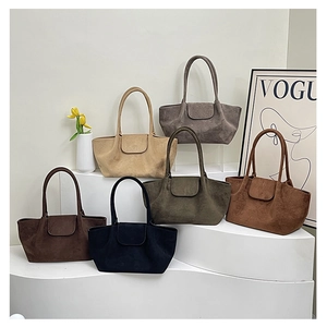 Bolsos tote de gamuza en seis colores otoñales exhibidos en un soporte blanco moderno