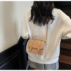Detail van een beige vintage crossbodytas met gouden klinknagels op een vrouwelijk model