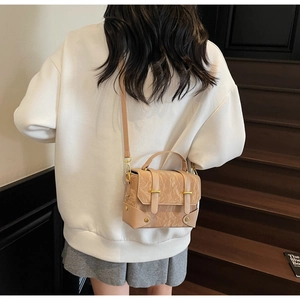 Detail van beige crossbodytas met plooitextuur en goudkleurige gespen gedragen door model