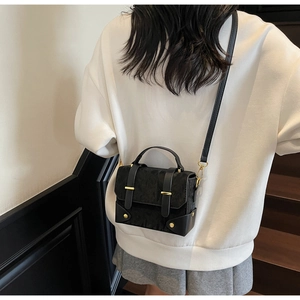 Detail van de getextureerde zwarte crossbodytas op een model met gouden gespaccenten