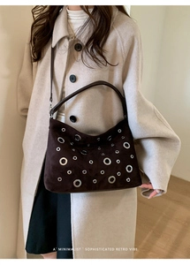 Detailed view of dark brown suede shoulder bag with decorative silver metal grommets