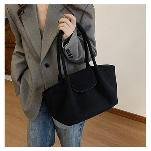 Detalle de bolso tote de ante negro con solapa semicircular y correa para el hombro