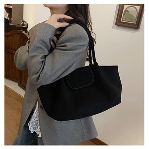Vista detallada de un bolso tote de ante negro con solapa decorativa sobre modelo